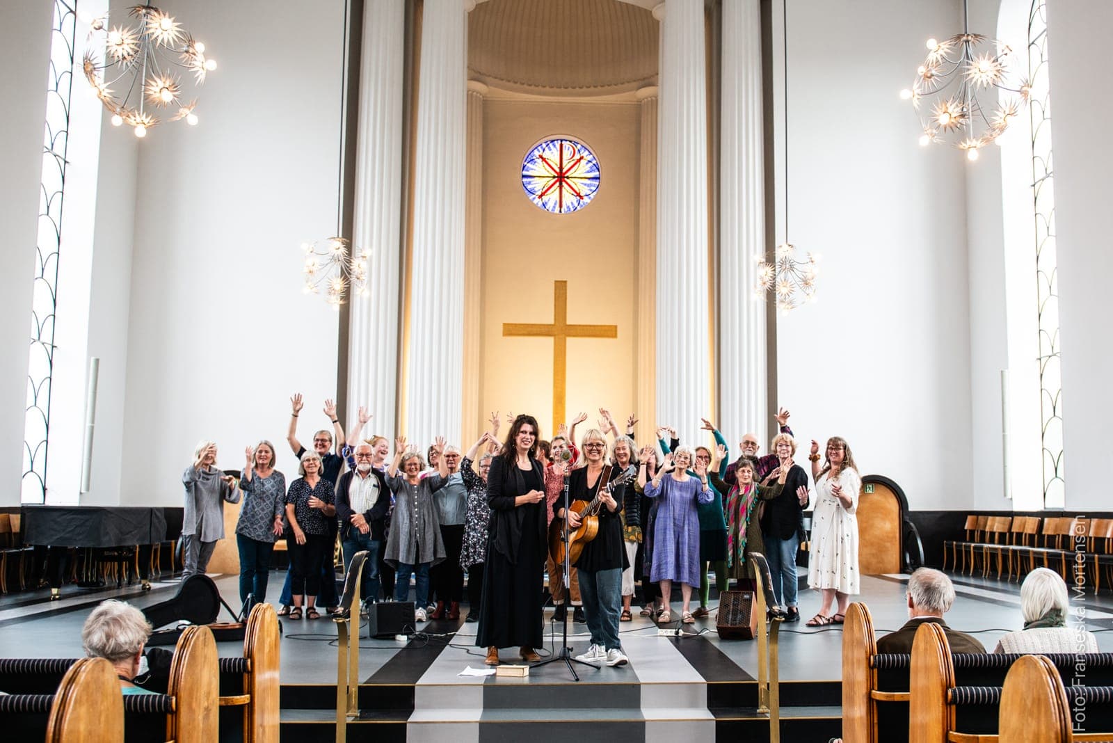 Musikere og sangere hilser publikum fra scenen i en lys kirke.
